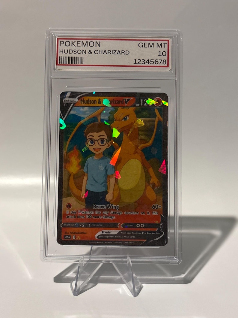 May include: A graded Pok&eacute;mon card featuring "Hudson & Charizard" with a GEM MT 10 grade. The card showcases a vibrant illustration of a boy and a Charizard, with the "Brave Wing" attack text visible. The card is encased in a clear protective holder.