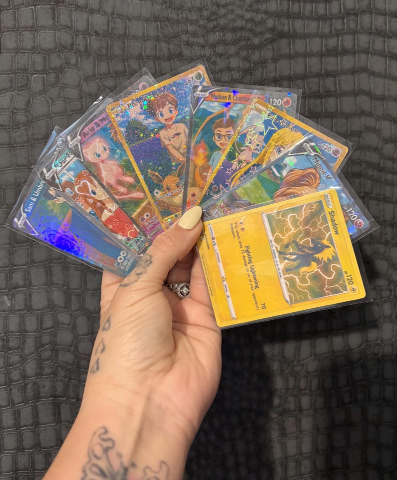 May include: A collection of holographic trading cards featuring various characters and the text "Ario & Me", "Sam & Umbrum", "Hudson & Charle", and "Minnie V". The cards are in protective sleeves, with a yellow card featuring a shadow graphic.