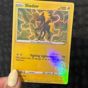 May include: A yellow Pok&eacute;mon trading card featuring a black and yellow silhouette of a horse-like creature with lightning effects. The card reads "Shadow" and "Fighting Lightning" with a damage value of 70.