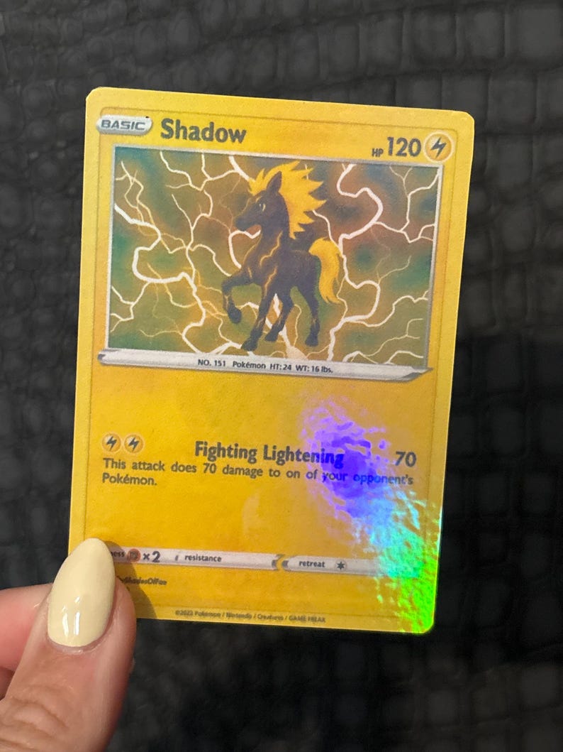 May include: A yellow Pok&eacute;mon trading card featuring a black and yellow silhouette of a horse-like creature with lightning effects. The card reads "Shadow" and "Fighting Lightning" with a damage value of 70.