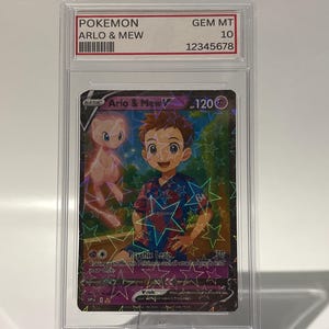 May include: A Pokemon trading card featuring "Arlo & Mew V" in a protective case. The card has a holographic background with star patterns. The text "POKEMON" and "GEM MT 10" are visible on the case. The card's illustration shows a boy and a pink Mew.