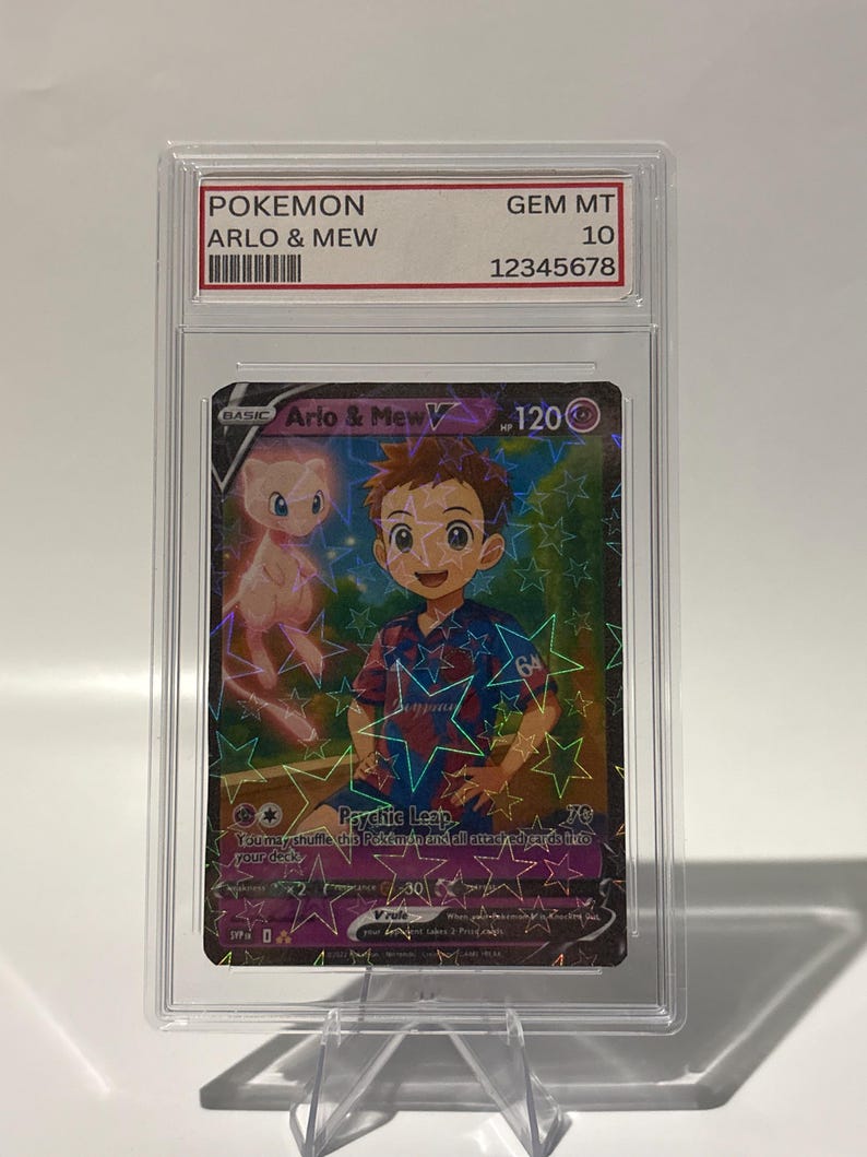May include: A Pokemon trading card featuring "Arlo & Mew V" in a protective case. The card has a holographic background with star patterns. The text "POKEMON" and "GEM MT 10" are visible on the case. The card's illustration shows a boy and a pink Mew.