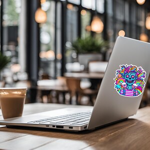 May include: A silver laptop computer with a colorful sticker of a blue cartoon character with a skull face surrounded by rainbows, clouds, and stars. The laptop is on a wooden table.