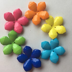 May include: Six colorful plastic flower-shaped buttons. The buttons are in a rainbow pattern, starting with orange, pink, yellow, green, blue, and ending with dark blue.