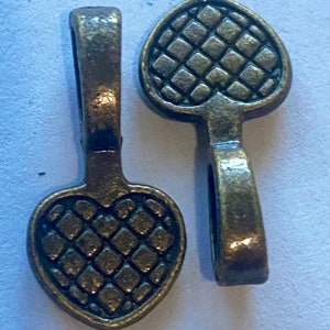 May include: Two antique bronze-colored heart-shaped pendants with a textured diamond pattern. Each pendant has a loop at the top for attaching to a chain or other jewelry component. The pendants are displayed on a light background.