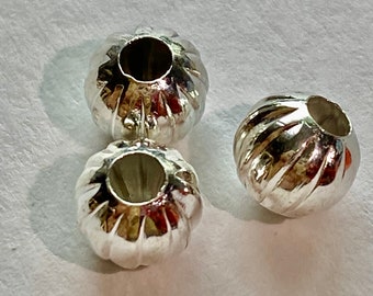 May include: Three silver-toned round beads with a ribbed texture and a hole in the center.