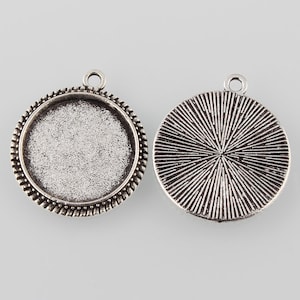 May include: Two silver-toned metal pendant trays, one with a smooth, round surface and the other with a textured, radial pattern. Both trays have a loop at the top for hanging.