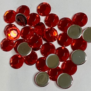 May include: A large assortment of red, round, flat-backed rhinestones. The rhinestones have a shiny, reflective surface.