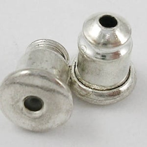 May include: Two silver earring backs, one with a flat back and the other with a rounded back.