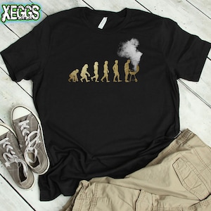 May include: Black t-shirt with a gold graphic of the evolution of man, ending with a man grilling. The graphic includes the text "Evolution of Man".