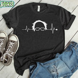 以下が含まれることがあります： 白い眼鏡と心拍線のついた人の顔の白いグラフィックが描かれた濃いグレーのTシャツ。グラフィックは、心拍線のついた人の顔のスタイリッシュな表現です。