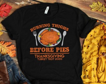 May include: Black t-shirt with a graphic of a Thanksgiving turkey on a plate with the text "Burning Thighs Before Pies Thanksgiving Turkey Trot 2020".
