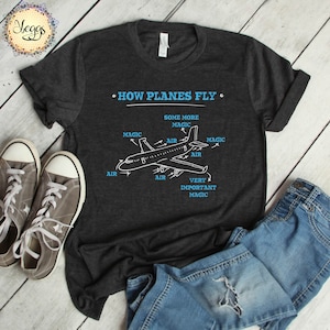 May include: A dark grey t-shirt with a white graphic of an aeroplane and the text "HOW PLANES FLY" with arrows pointing to different parts of the plane labelled "AIR" and "MAGIC".