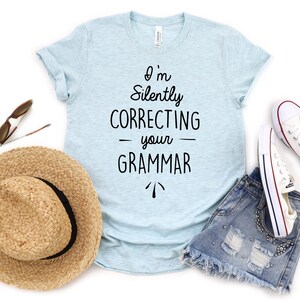 May include: A light blue t-shirt with the text "I'm Silently Correcting Your Grammar" in black lettering.