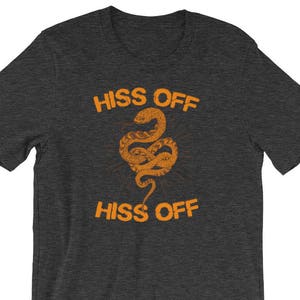 Puede incluir: Una camiseta gris oscuro jaspeada con un gr&aacute;fico de una serpiente y el texto "Hiss Off" impreso en naranja.