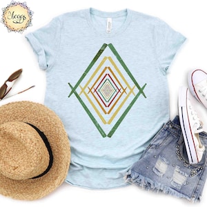 May include: A light blue t-shirt with a geometric design in shades of green, yellow, orange, and red. The design is a diamond shape with multiple lines intersecting to create a pattern.