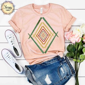 May include: A peach colored t-shirt with a geometric design in shades of green, yellow, orange, and red. The design is a series of concentric squares.