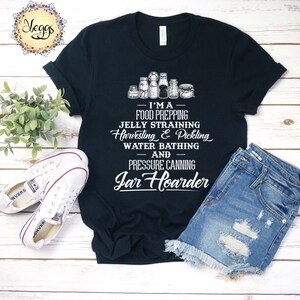 Puede incluir: Una camiseta negra con un gr&aacute;fico blanco que dice "Soy un preparador de alimentos, un colador de jalea, una cosecha y un encurtido, un ba&ntilde;o de agua y un enlatador a presi&oacute;n de tarros". El gr&aacute;fico tambi&eacute;n incluye una fila de tarros.