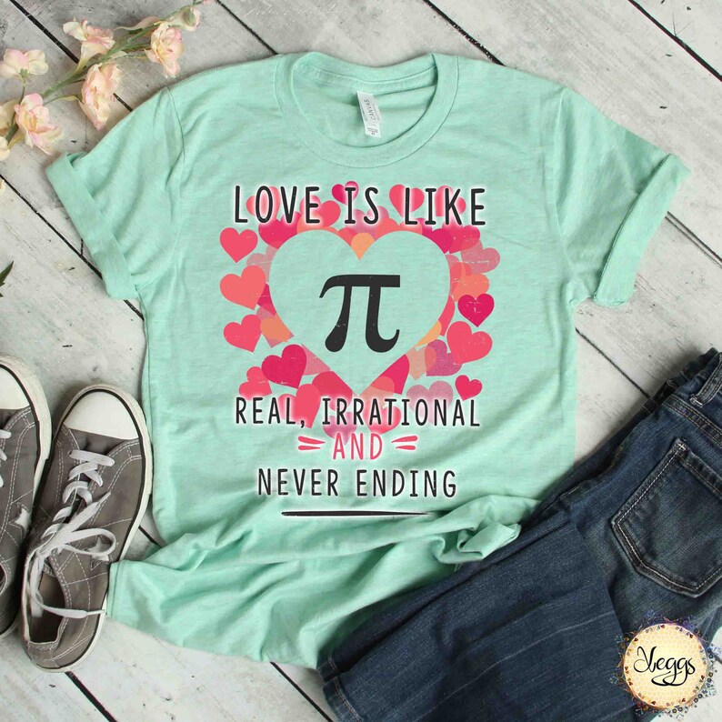 Pu&ograve; includere: Una maglietta verde chiaro con un design a forma di cuore rosa che presenta il simbolo matematico pi. Il testo "Love is like Pi, Real, Irrational and Never Ending" &egrave; stampato sulla maglietta.