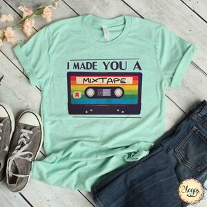 May include: A light green t-shirt with the text "I made you a mixtape" and a vintage cassette tape graphic. The cassette tape has rainbow colored stripes.