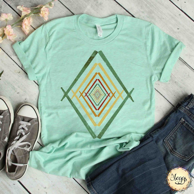 May include: A light green t-shirt with a geometric design in shades of green, yellow, orange, and red. The design is a series of overlapping diamonds, creating a visual illusion of depth.