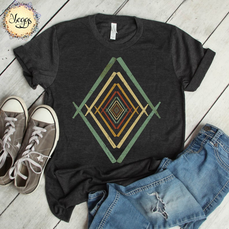 May include: A dark grey t-shirt with a geometric design in shades of green, yellow, orange, and red. The design is a series of overlapping diamonds, creating an optical illusion effect.