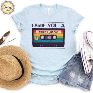 May include: A light blue t-shirt with the text "I made you a mixtape" and a retro cassette tape graphic. The cassette tape has rainbow colored stripes.
