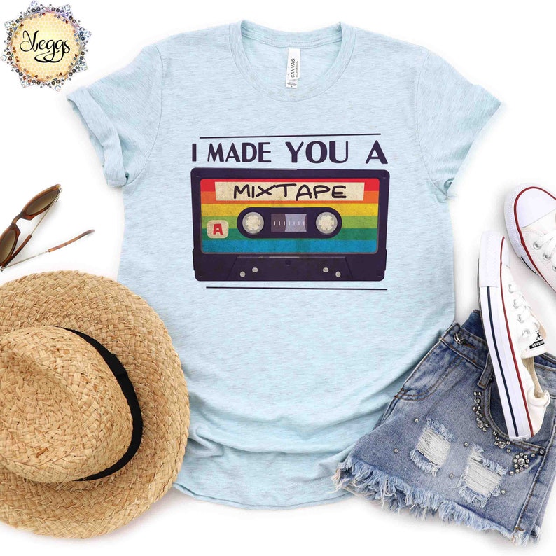 May include: A light blue t-shirt with the text "I made you a mixtape" and a retro cassette tape graphic. The cassette tape has rainbow colored stripes.