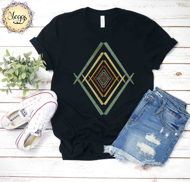 May include: A black t-shirt with a geometric design in shades of green, yellow, and orange. The design is a series of overlapping diamonds that create an optical illusion.