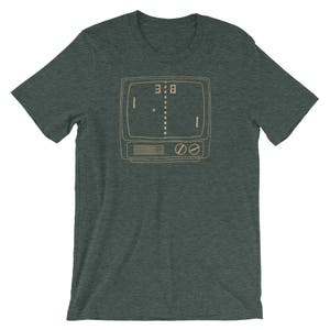 Puede incluir: Una camiseta verde oscuro con una ilustraci&oacute;n de estilo vintage de un juego de arcade retro. El juego se muestra en una pantalla de televisi&oacute;n con el marcador 3:8.