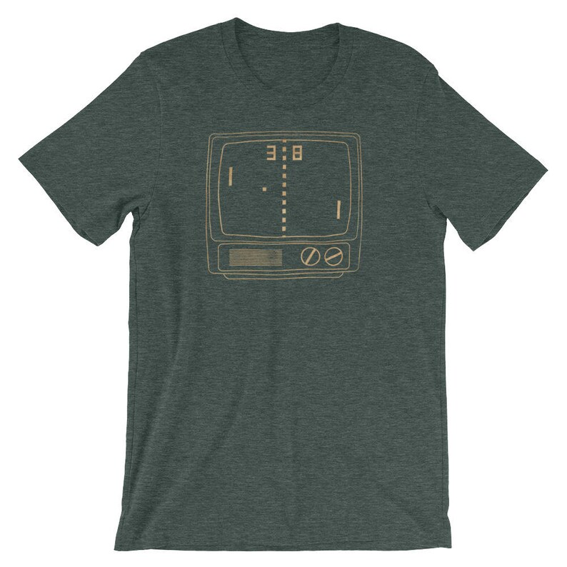 Puede incluir: Una camiseta verde oscuro con una ilustraci&oacute;n de estilo vintage de un juego de arcade retro. El juego se muestra en una pantalla de televisi&oacute;n con el marcador 3:8.