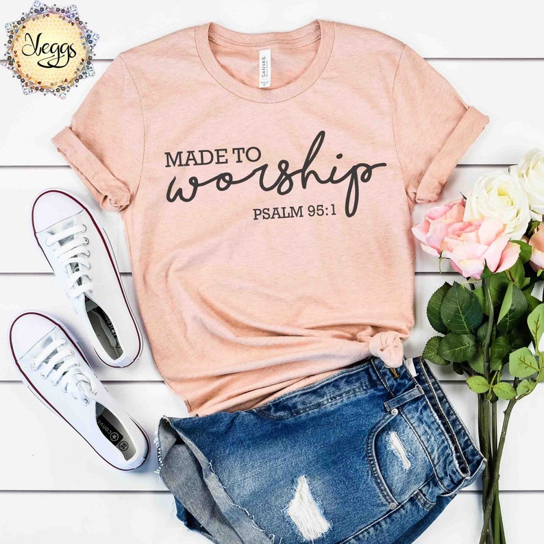 May include: A peach-colored t-shirt with the text "MADE TO worship" and "PSALM 95:1" in black lettering. The shirt is laid out on a white surface with a pair of white sneakers and a pair of blue denim shorts.
