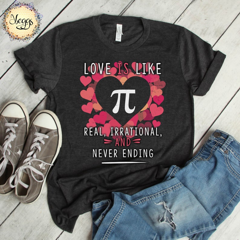 Pu&ograve; includere: Una maglietta grigia scura con il testo "LOVE IS LIKE" e una grafica a forma di cuore che contiene il simbolo matematico di pi. Il testo sotto la grafica dice "REAL, IRRATIONAL, AND NEVER ENDING".