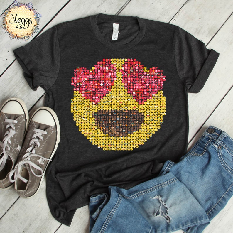 Puede incluir: Camiseta gris oscuro con un gran dise&ntilde;o de cara emoji. La cara emoji est&aacute; compuesta por emojis m&aacute;s peque&ntilde;os, con gafas de sol rosas en forma de coraz&oacute;n y una cara amarilla. Zapatillas grises y vaqueros azules est&aacute;n al lado de la camiseta.