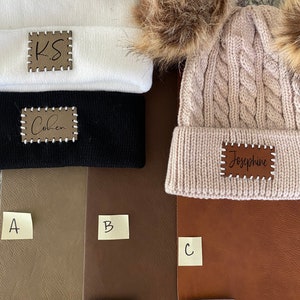 Peut inclure: Trois bonnets en blanc, noir et beige avec des &eacute;cussons en cuir personnalis&eacute;s. Le bonnet blanc porte l'inscription "KS". Le bonnet noir porte l'inscription "Cohen". Le bonnet beige porte l'inscription "Josephine".