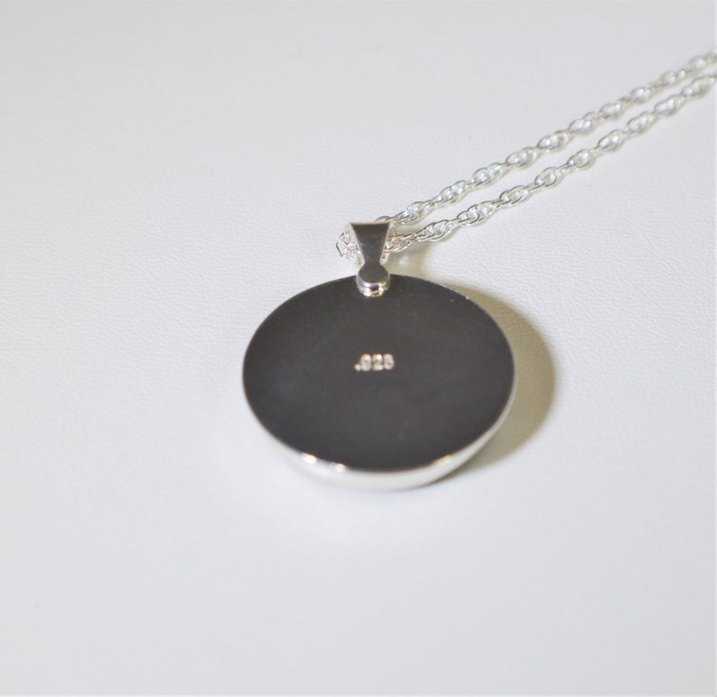 May include: Silver pendant necklace with a round disc charm. The back of the charm has the inscription .925.
