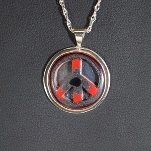 May include: A silver chain necklace with a round pendant featuring a black and red peace sign.