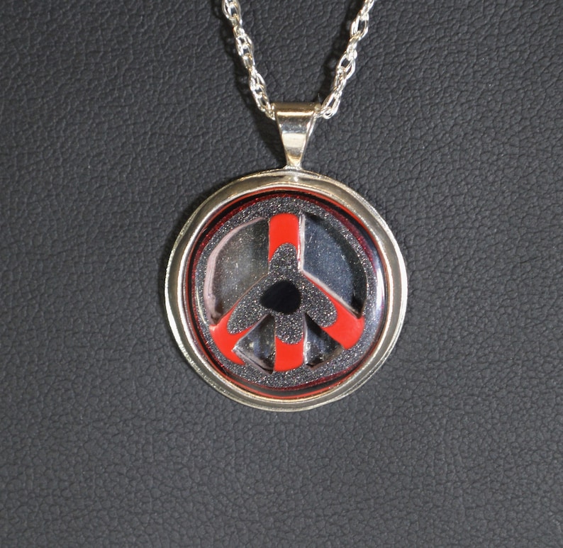 May include: A silver chain necklace with a round pendant featuring a black and red peace sign.