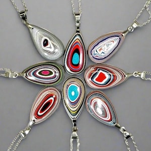 May include: Eight teardrop-shaped pendants arranged in a circular pattern, each featuring layered, multi-colored concentric rings. The pendants are crafted from polished material with vibrant bands of red, blue, white, black, and silver, suspended on silver chains.