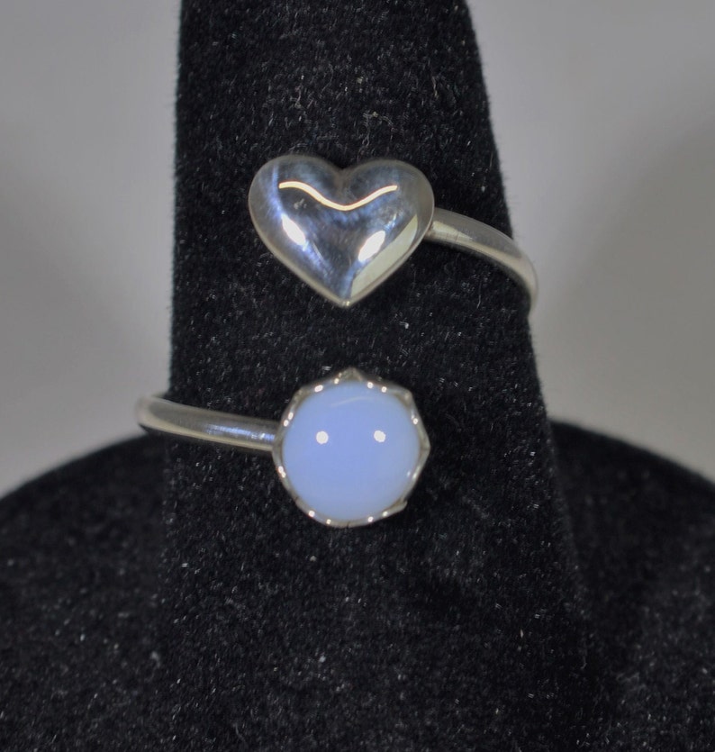 May include: Two silver rings with a heart-shaped stone and a round, light blue stone.