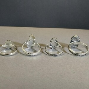 May include: Four silver rings with different designs. Each ring has a raised oval stone in the center.
