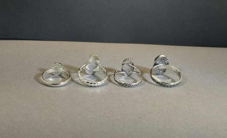May include: Four silver rings with different designs. Each ring has a raised oval stone in the center.