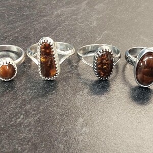 May include: Four silver rings with different brown agate stones. The rings are set in silver and have a variety of styles.