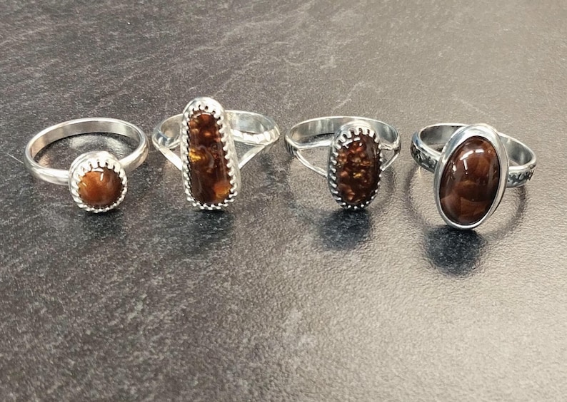 May include: Four silver rings with different brown agate stones. The rings are set in silver and have a variety of styles.