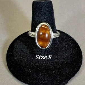 May include: A silver ring with an oval-shaped brown gemstone. The ring is on a black ring display stand. Size 8.