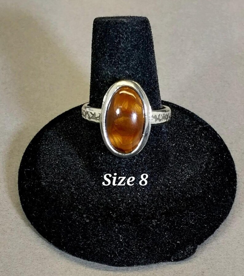 May include: A silver ring with an oval-shaped brown gemstone. The ring is on a black ring display stand. Size 8.