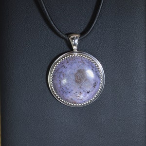 May include: A silver pendant necklace with a round, purple and gray stone set in a silver bezel. The stone has a swirling pattern.