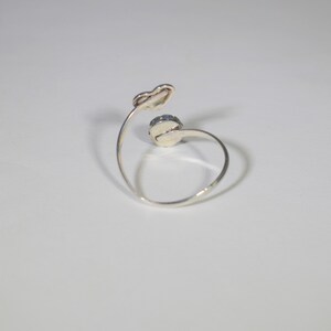 May include: A silver ring featuring a single round blue gemstone. The ring has a curved band and a heart-shaped detail.