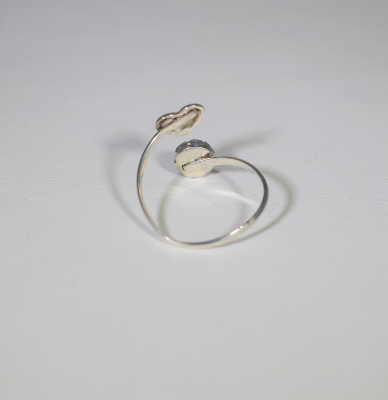 May include: A silver ring featuring a single round blue gemstone. The ring has a curved band and a heart-shaped detail.