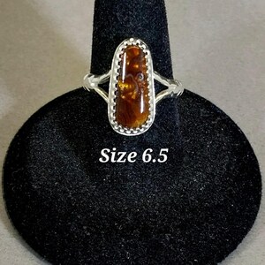 May include: A silver ring with a brown and gold oval gemstone set in a silver bezel. The ring is size 6.5.